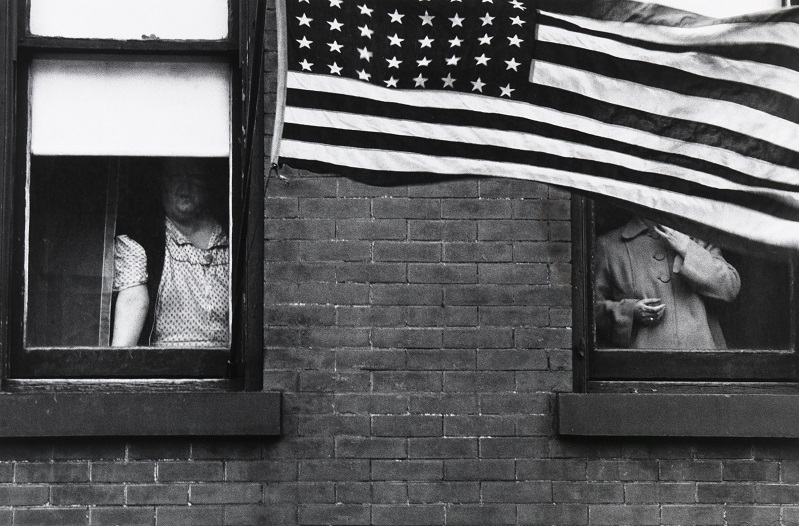 Photograph of people looking out of a building with a large American flag