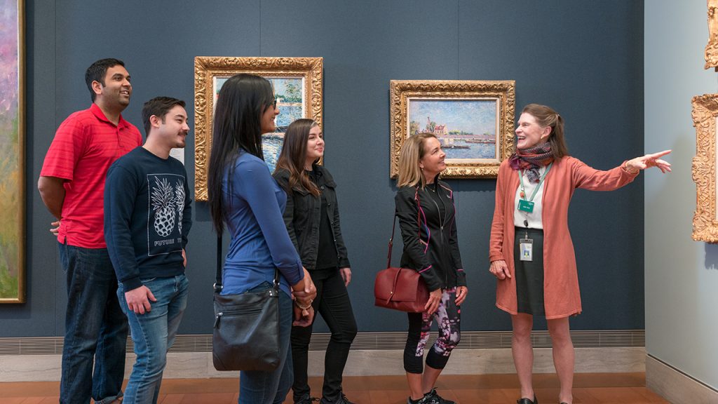 A museum guide shares information about a painting in a gallery for a group of young people.