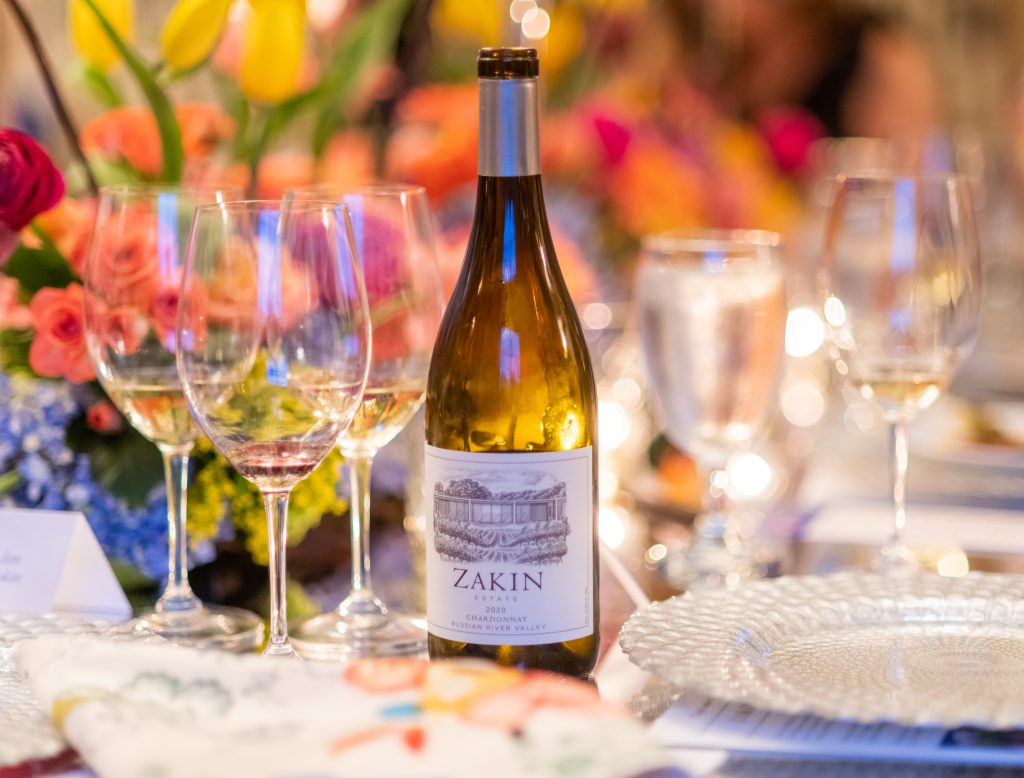 A bottle of Chardonnay stands on a table, surrounded by several glasses of wine.