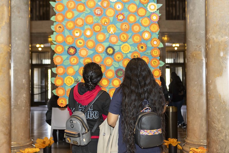 Two guests look at a yellow day of the dead alter with handwritten notes to loved ones.