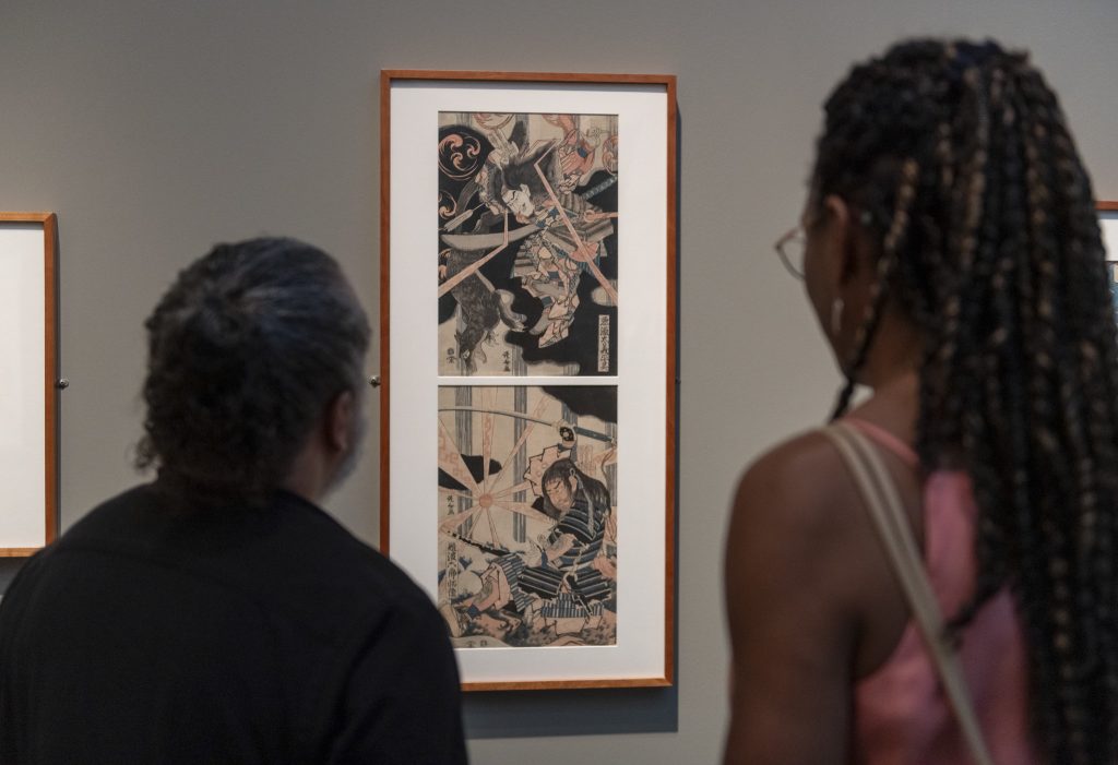 Two people gaze at a print in the Nelson-Atkins exhibition Hokusai: Waves of Inspiration from the Museum of Fine Arts, Boston.