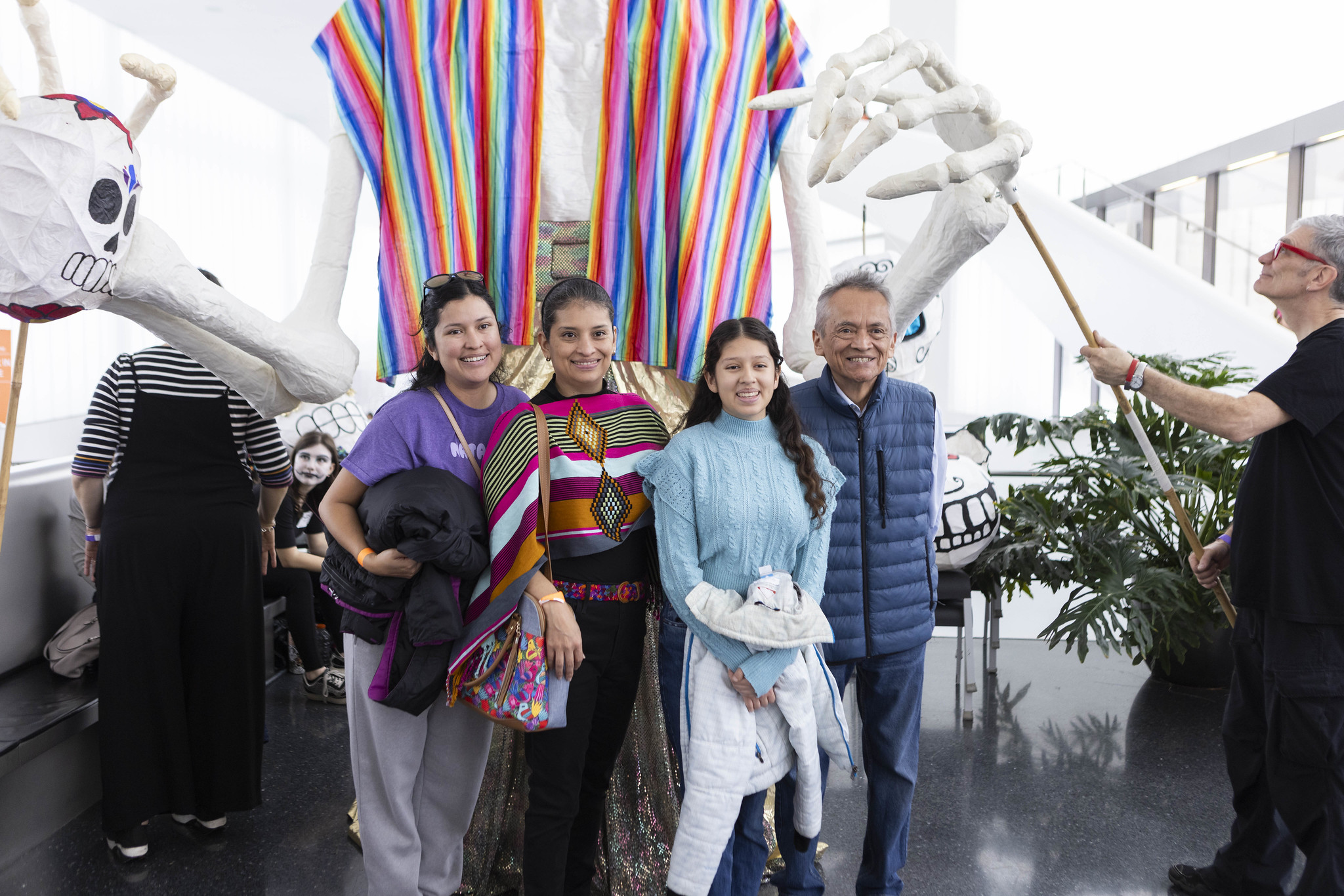 A family poses in front of a large skeleton puppet at the Nelson-Atkins Dia de los Muertos Festival