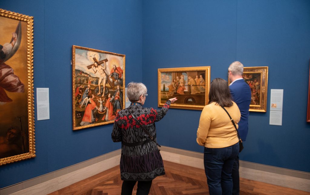 A Nelson-Atkins docent shares information about a painting with guests in a gallery,