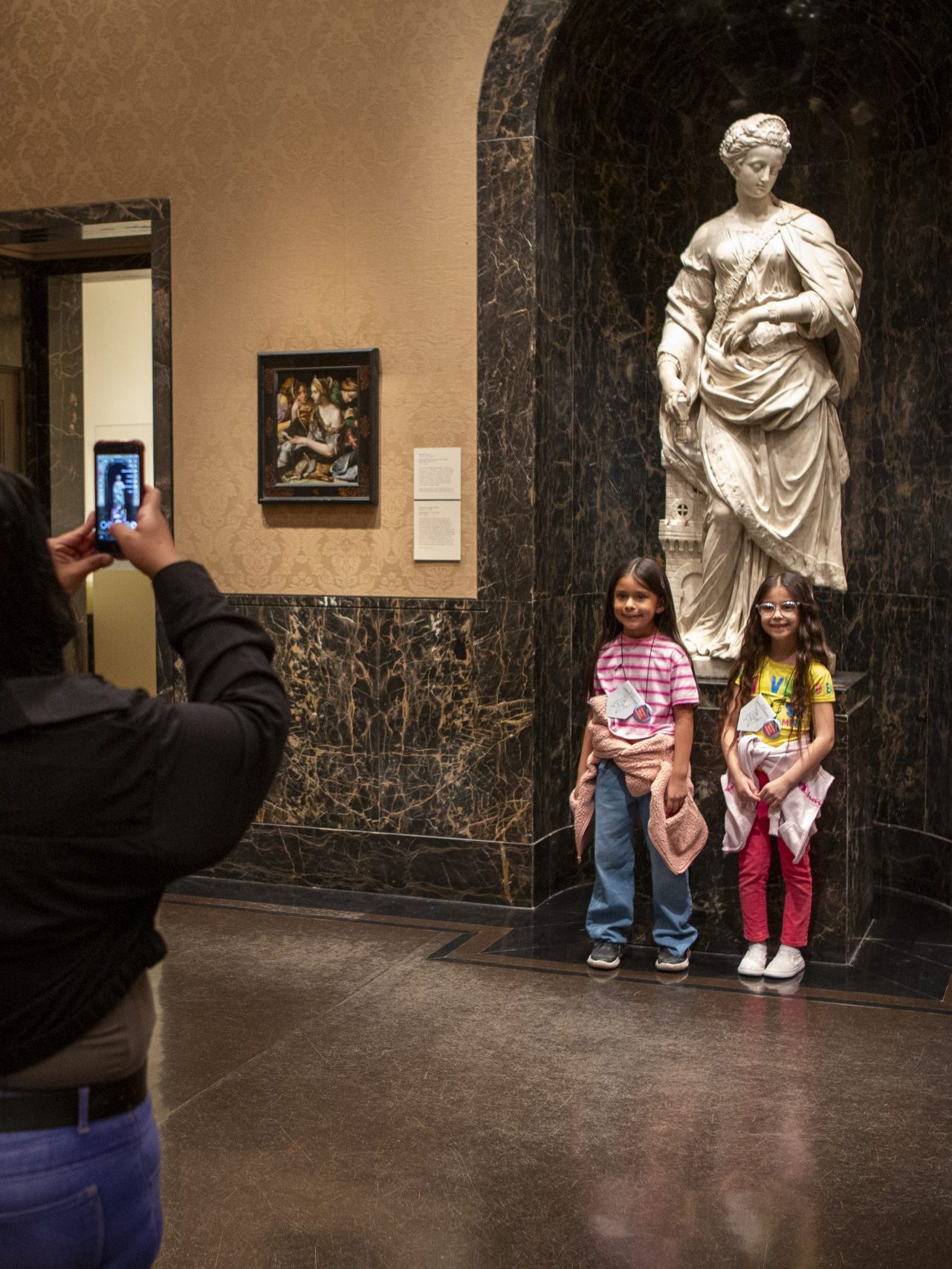 Two girls pose for a photo in front of a statue in a gallery at The Nelson-Atkins Museum of Art.