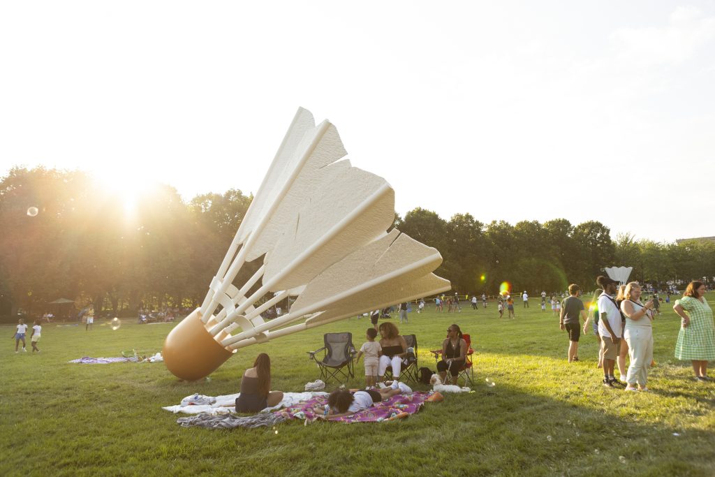 A family lounges on a picnic blanket near a Shuttlecock sculpture on the south lawn of the Nelson-Atkins.