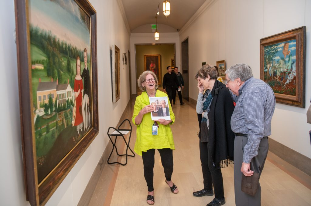 A Nelson-Atkins Docent laughs with guests as she describes context for a painting in a gallery.