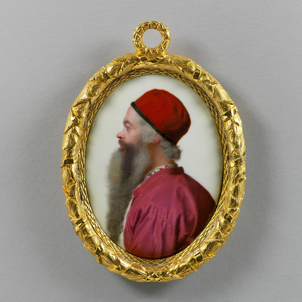 A photograph of a detailed golden frame surrounding a side view of a portrait of a man. He wears a red cap and has a with a long gray and brown beard.