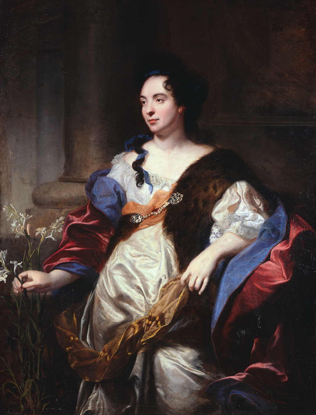 A light-skinned, dark-haired woman, painted from the knees up, stands leaning on her bent left arm against a stone ledge. She wears a white dress with a yellow sash and a red cloak lined in blue. Along her left shoulder is a brown and black-spotted animal pelt pinned with a jewelled clasp. She plucks a long stem off a white-flowered plant.