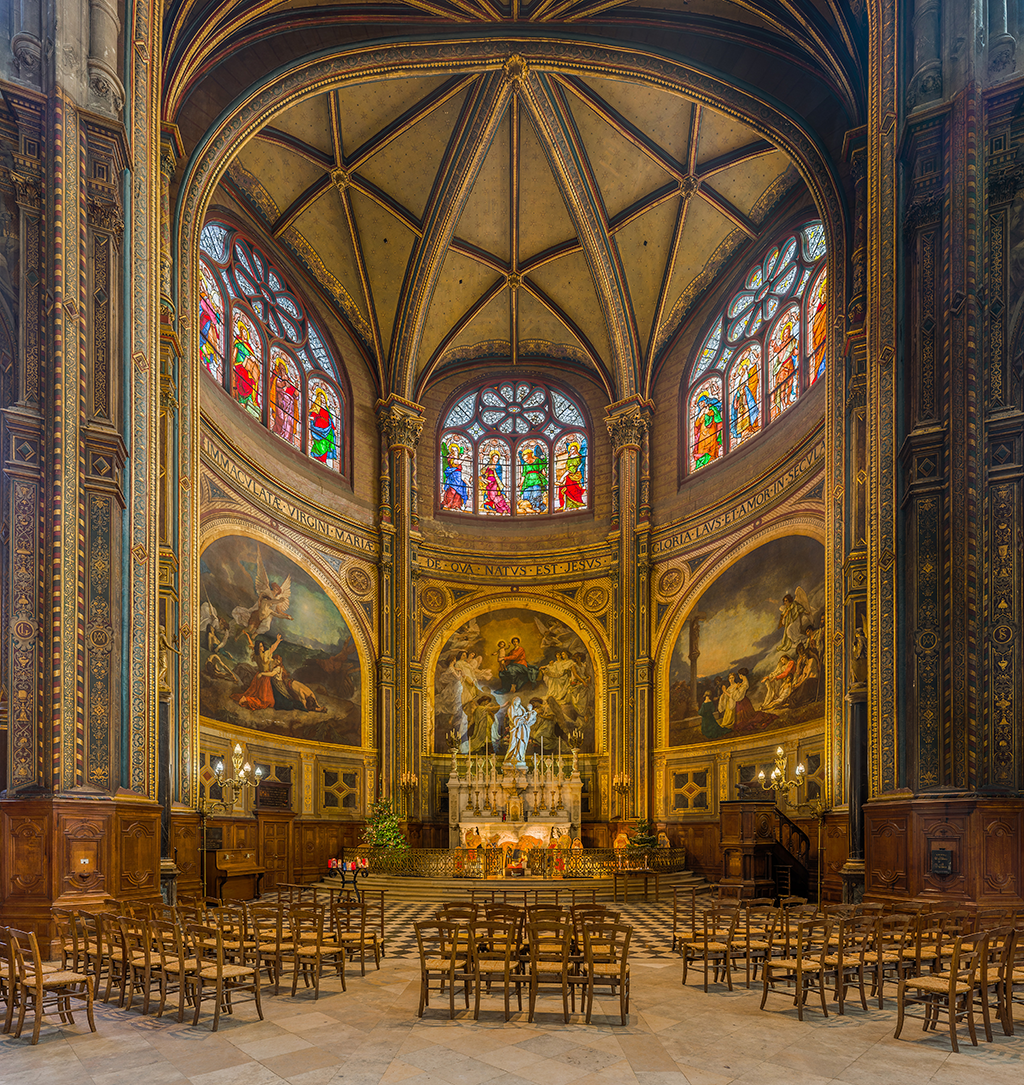 A large symmetrical and open room filled with decorations and pillars. There are three colorful stained-glass windows portraying saints. The walls are curved and have Latin text written on the three panels. Under them are three paintings depicting biblical events. On the ground are rows of wooden chairs on a checkered floor facing a stone sculpture surrounded by candles.