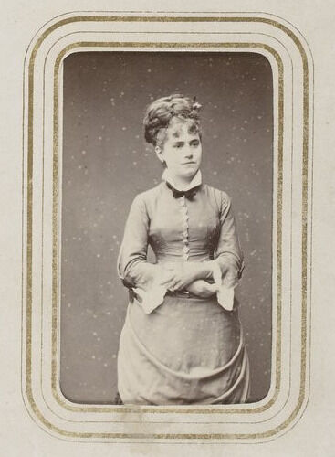 A photograph of a woman wearing a dress with her arms folded over her lower waist.