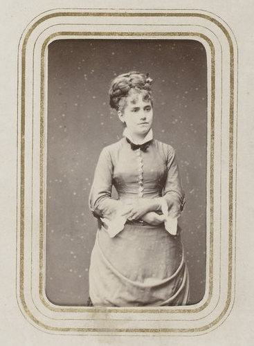 A photograph of a woman wearing a dress with her arms folded over her lower waist.