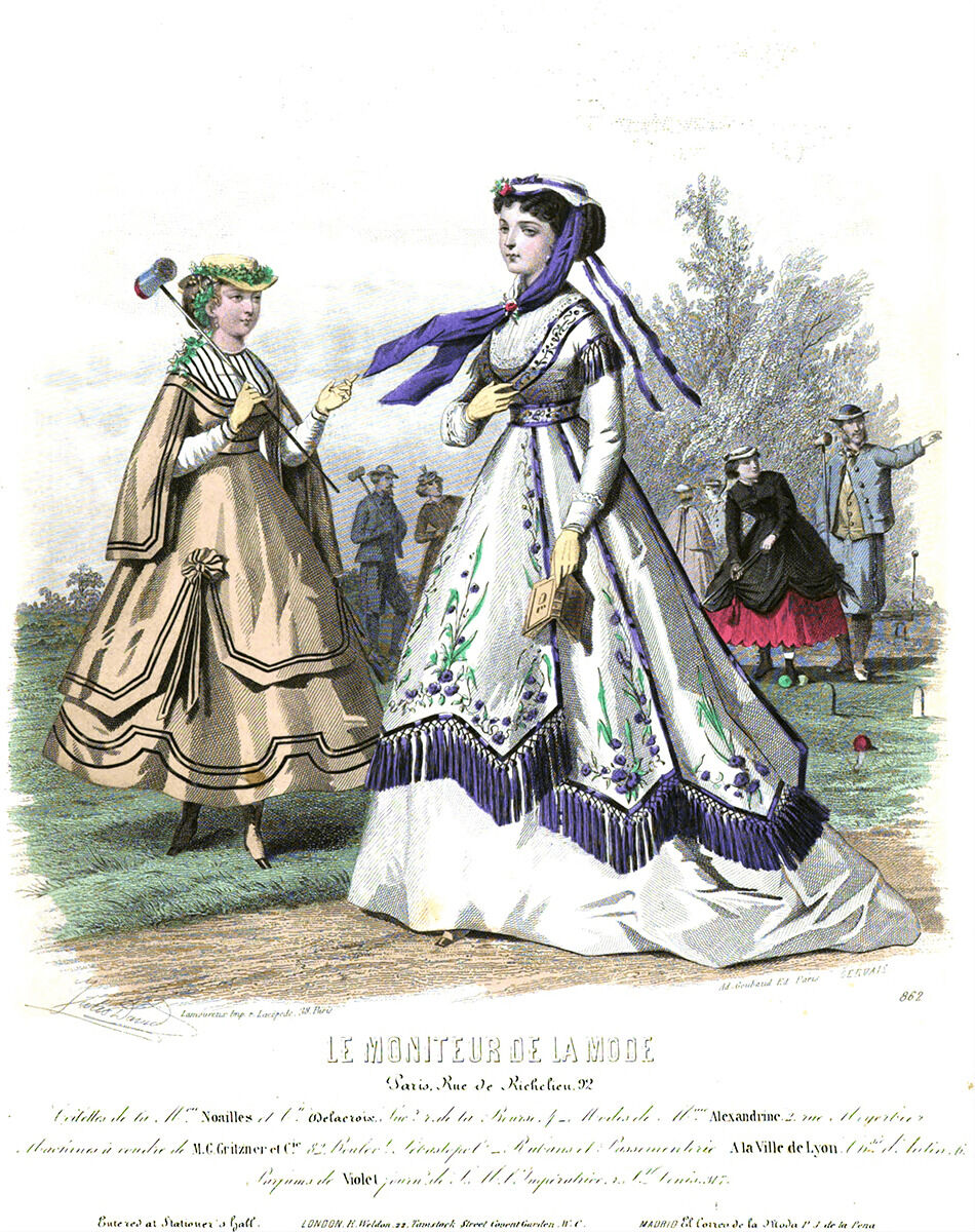 An image of a woman wearing a large white dress with purple tassels and a scarf. Another woman stands behind her wearing a yellow dress and she is carrying a wooden mallet. In the background there are people with mallets hitting colorful balls.