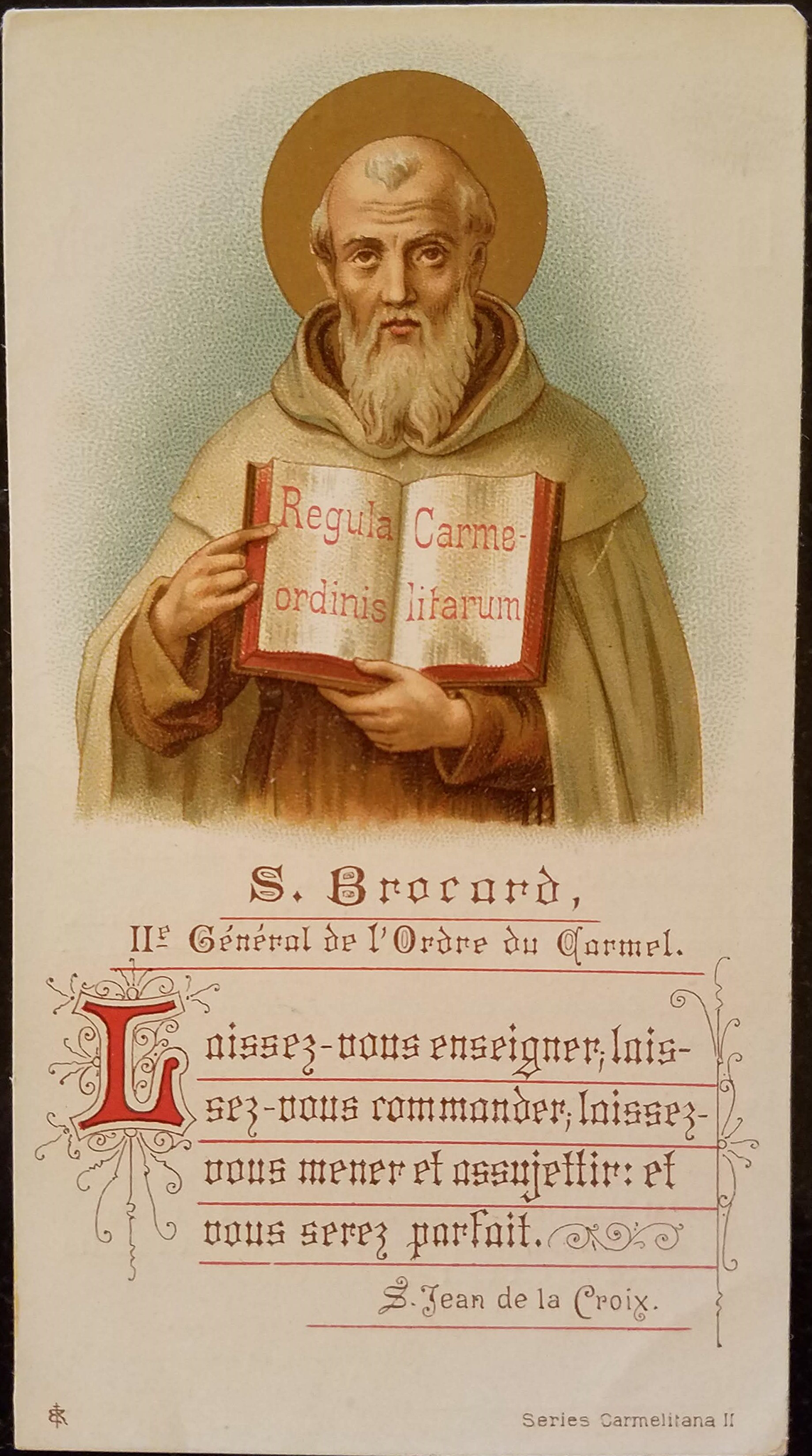 A card depicting an older man holding an open book and uses his right hand to point at the words written on it. The words read &ldquo;Regula Carme-ordirus litarum.&rdquo; The older man having gray hair around his head with a long white beard. He wears a long white cloak with a hood and a brown shirt underneath. Behind him is an orange circle. Under him is red letters written.