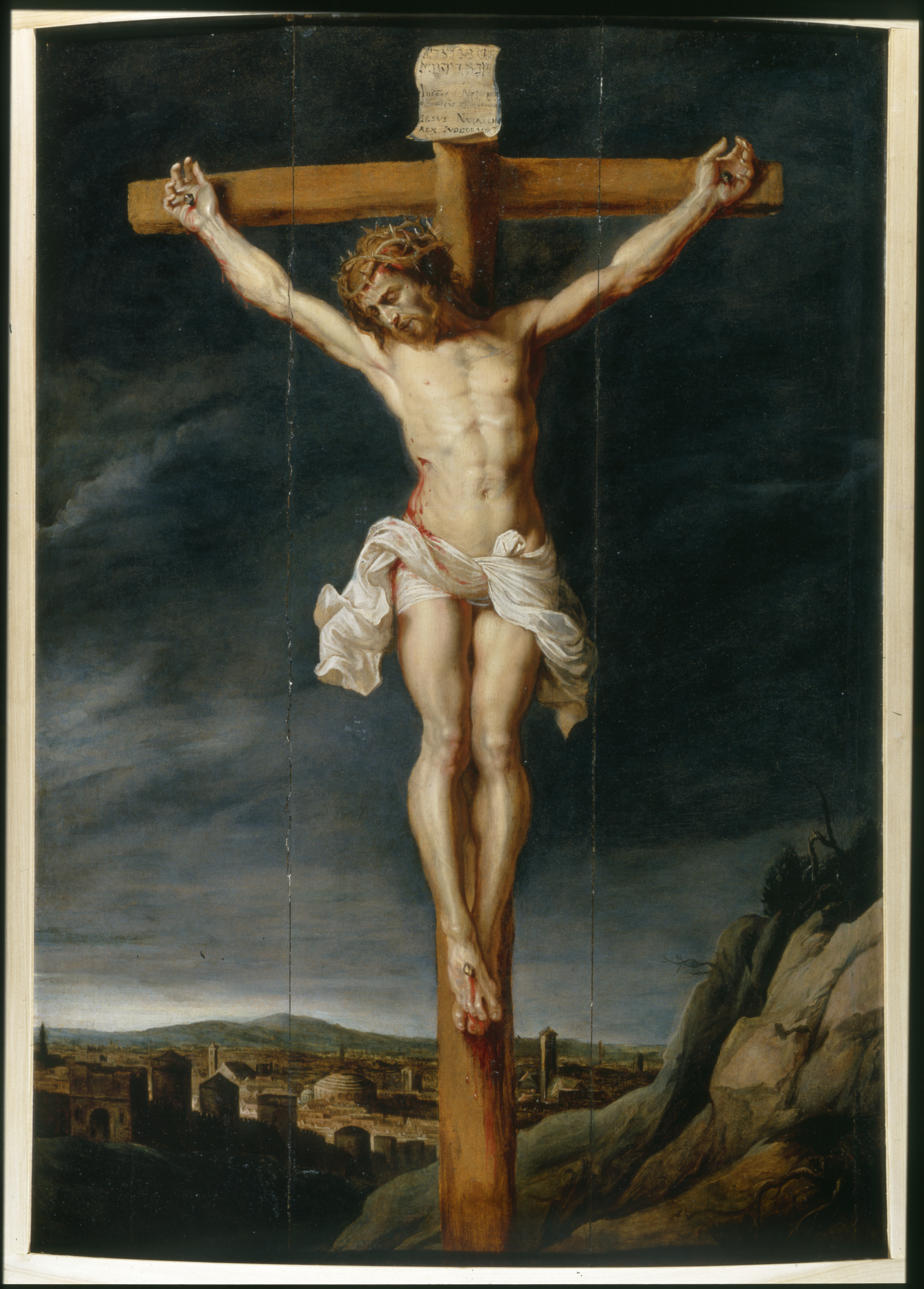 An image depicting a man with his hands and feet nailed to a wooden cross. The man wears a crown of thorns, and his head is tilted downward. On his body is a stab wound with blood pouring out onto the white cloth which is wrapped along his waist.