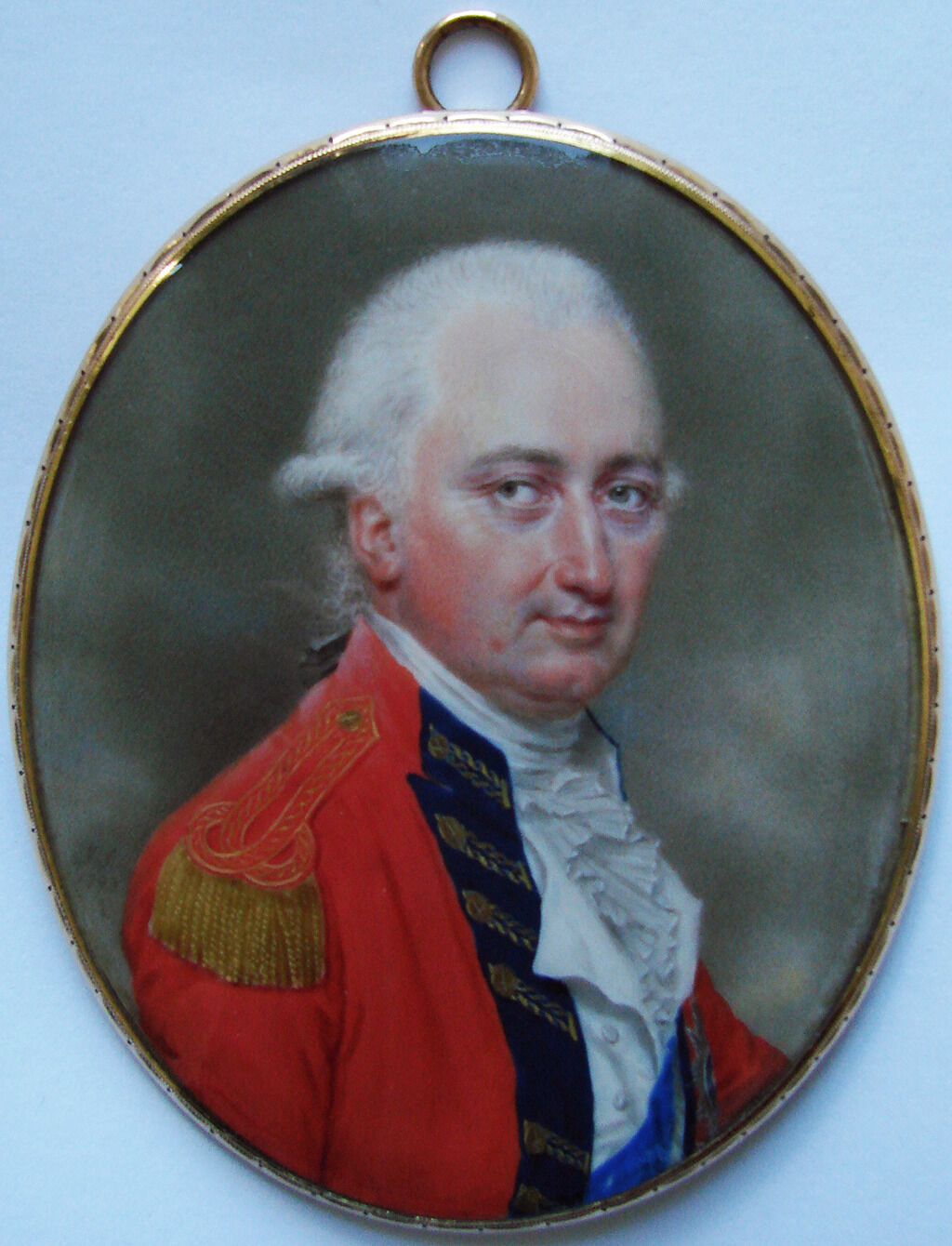Portrait miniature of a light-skinned man with powdered hair wearing a red military coat before a gray sky background.